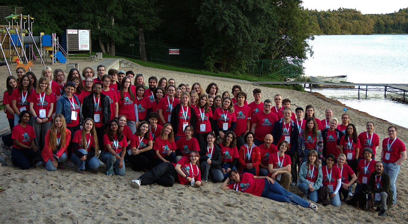 Biotechnology Summer School participants and speakers in matching pink shirts gathered beside the lake in Szarlota, Poland.